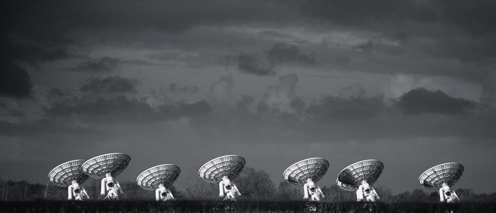 A row of white antenna dishes beneath a dark, stormy evening sky