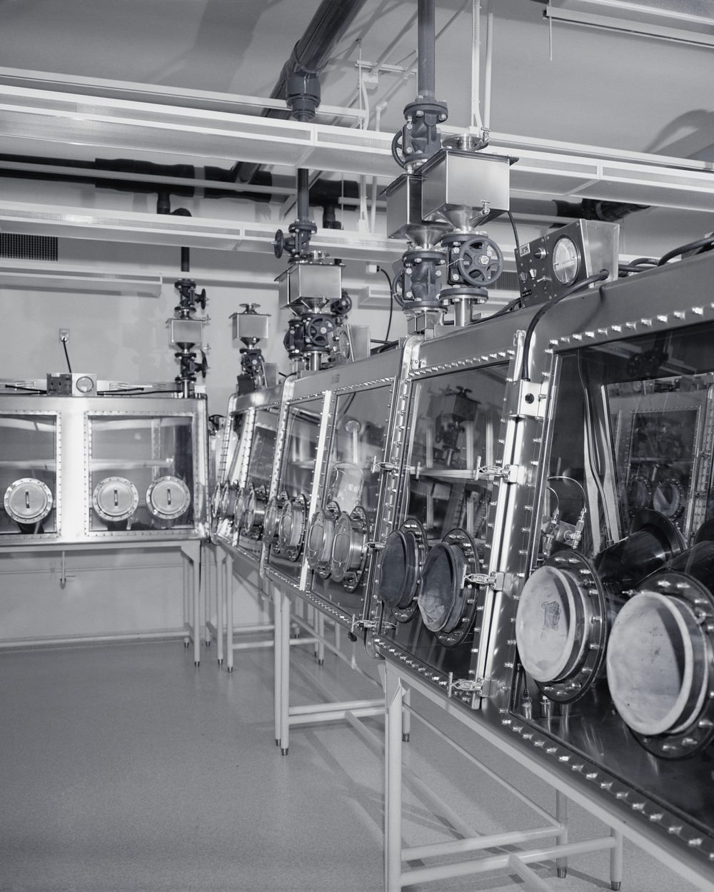 Empty laboratory lined with sealed steel glovebox cabinets and round glove ports