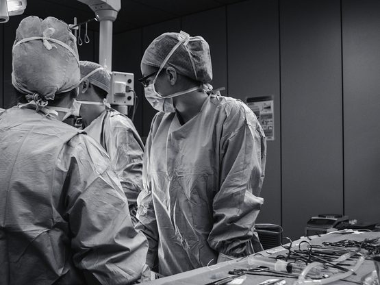 Surgical team in gowns, caps and masks preparing at an instrument table