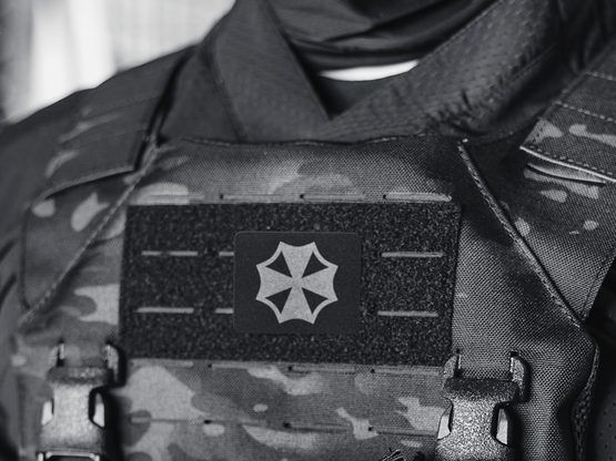 Operator in a neck gaiter and camouflage plate carrier, a white emblem patch on its identity panel