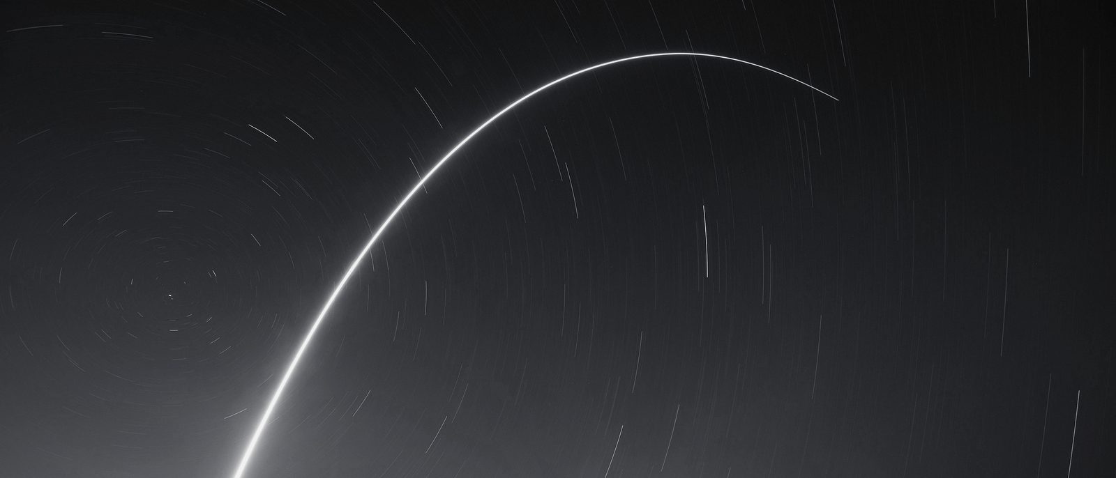 A single long-exposure launch trail arcing across a night sky of star trails